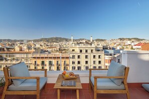 Um terraço com duas cadeiras de madeira, uma mesa com uma bandeja de comida e vista para a cidade.