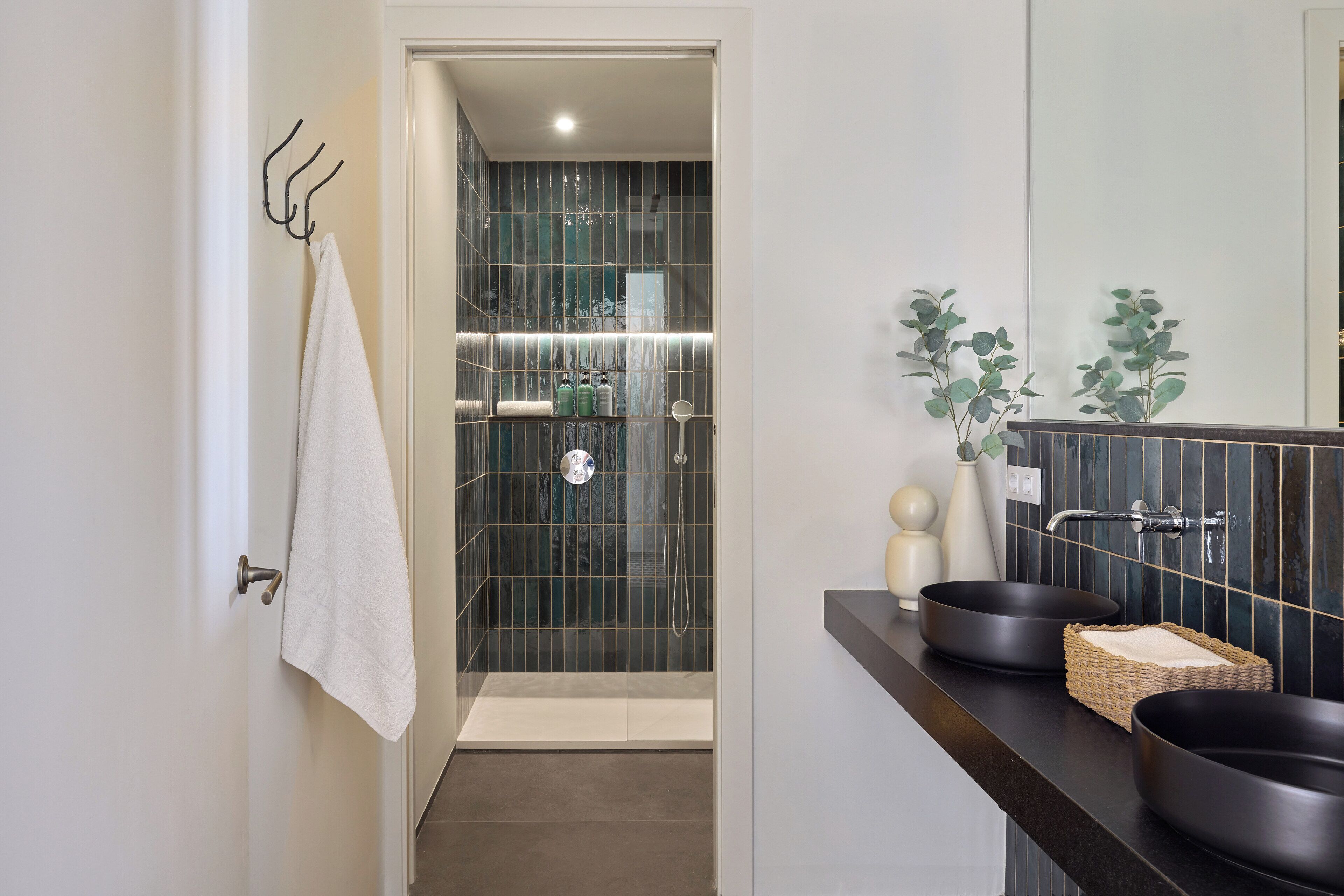 Un baño moderno con ducha, dos lavamanos negros y un espejo.