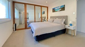 A bedroom with a bed, a nightstand, a mirror, and a wardrobe. - Gobsmacking Views 6 with Direct Beach Access (Cronulla)