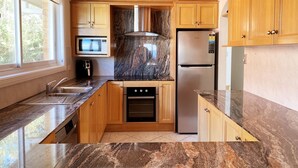 A modern kitchen with wooden cabinets, a granite countertop, a built-in oven, a stainless steel refrigerator, and a microwave. - Gobsmacking Views 6 with Direct Beach Access (Cronulla)