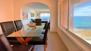 A dining area with a glass table, black chairs, and a view of the ocean through a large window. - Gobsmacking Views 6 with Direct Beach Access (Cronulla)