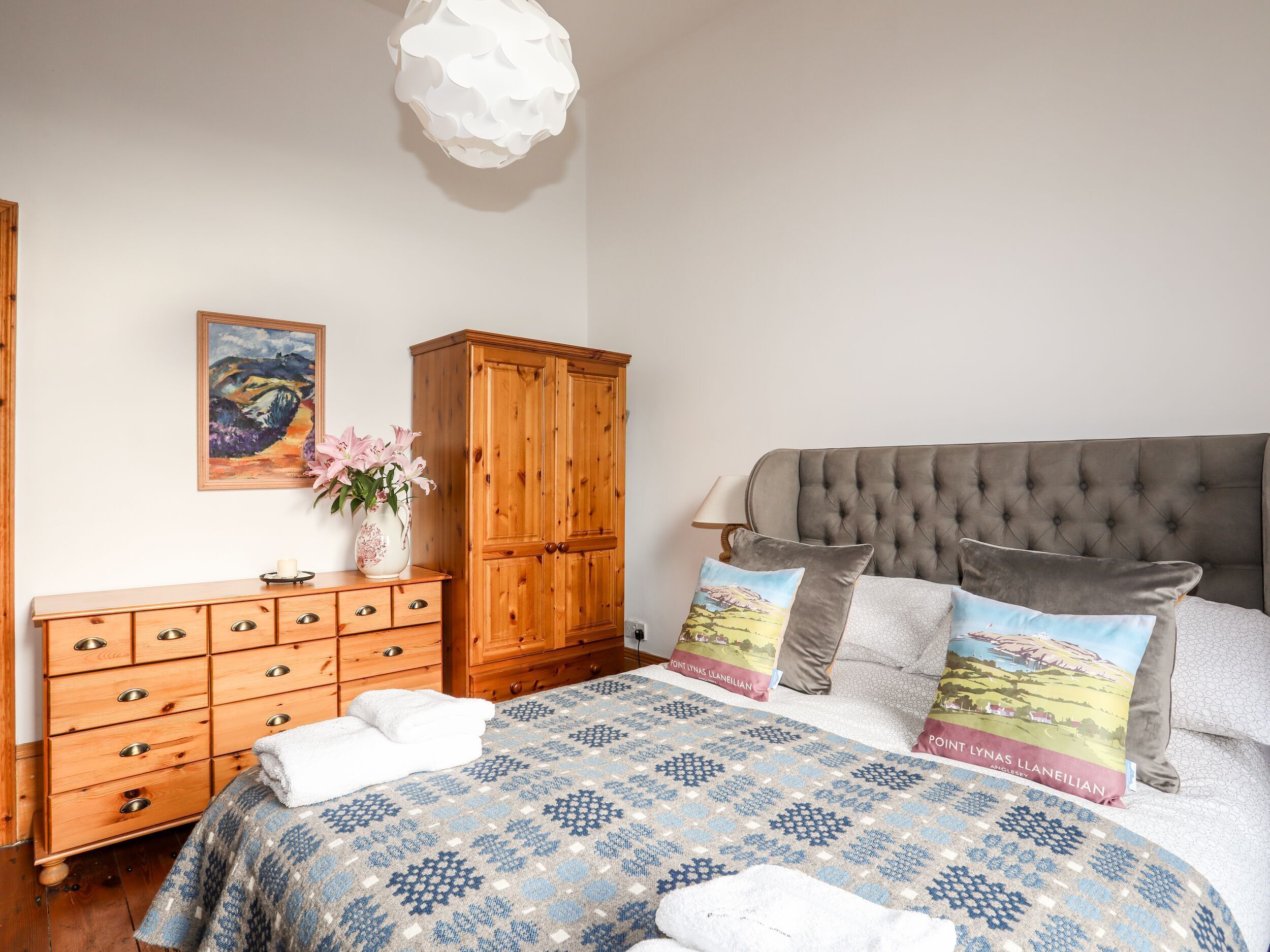 Una camera da letto con un letto, una cassettiera in legno, un armadio, un quadro e un vaso con fiori.