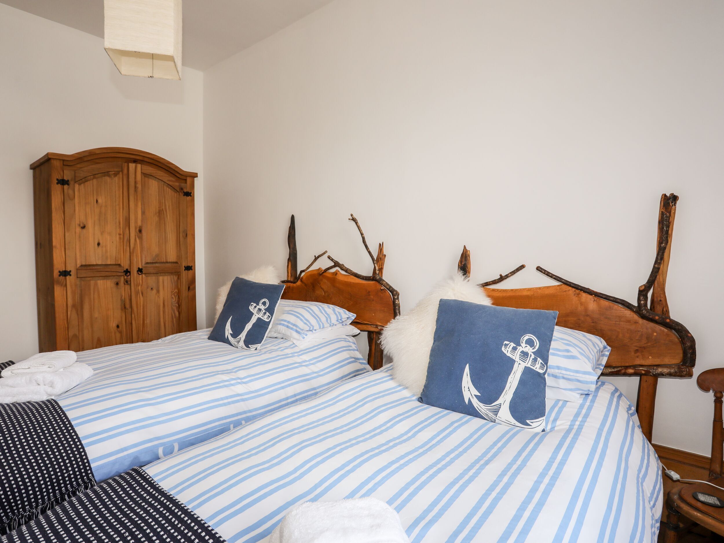 Cama doble con ropa de cama a rayas y dos almohadas con diseños de anclas, un armario de madera y un cabecero rústico.