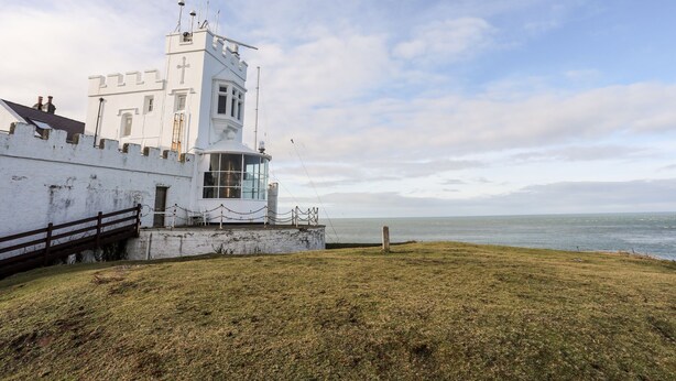 Un bâtiment blanc avec une tour, une pelouse devant et une vue sur la mer.