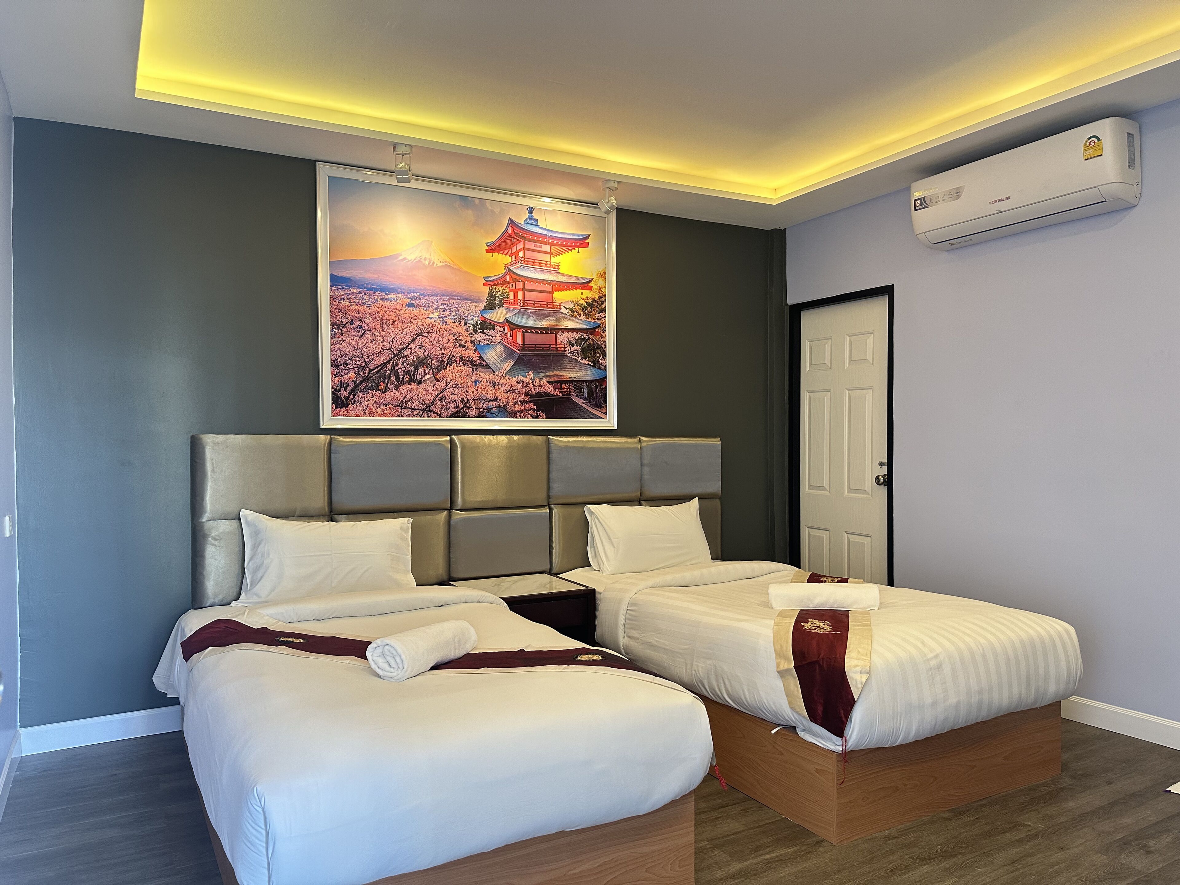 A hotel room with two beds, a large framed picture of a traditional building, and an air conditioning unit on the wall.