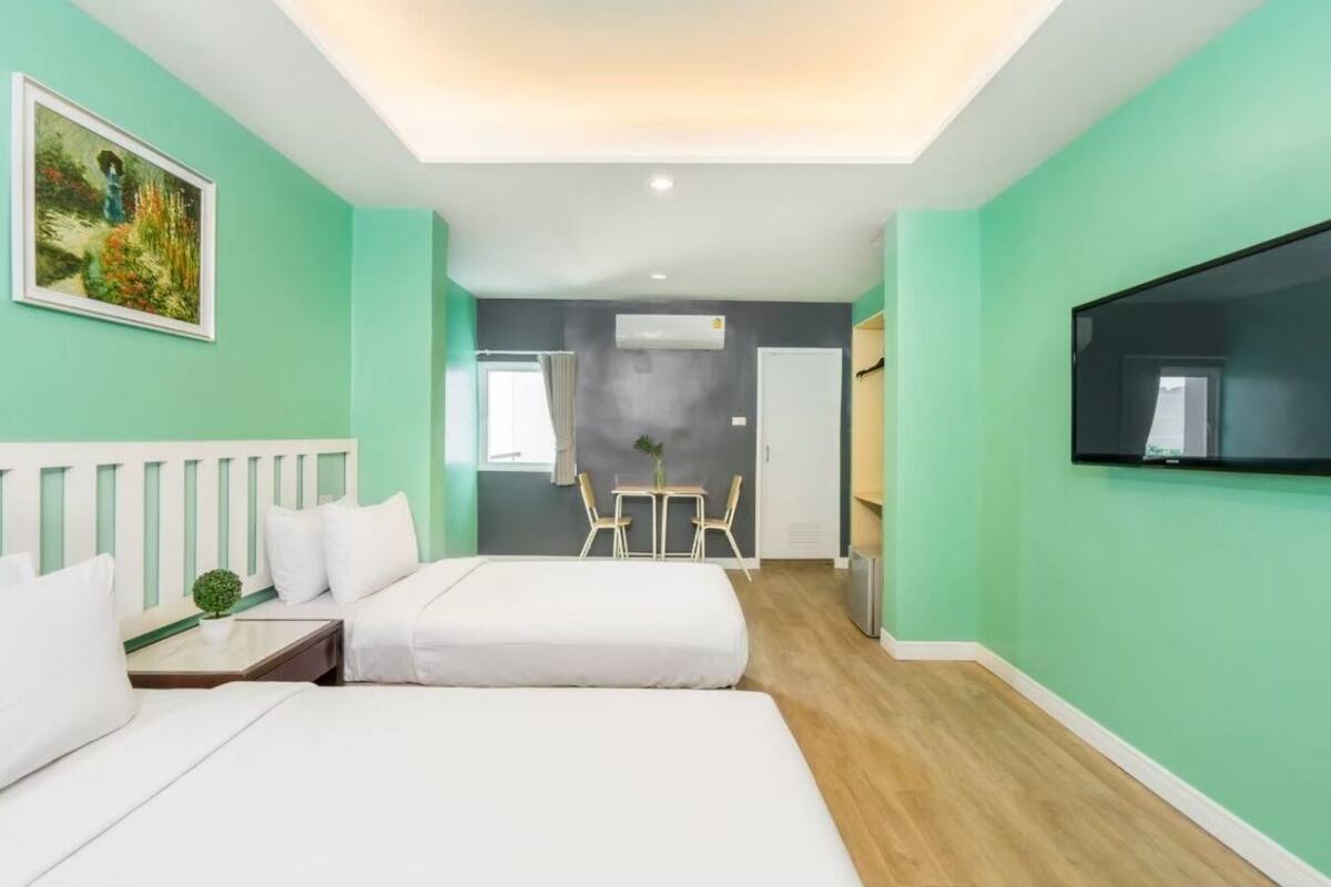 Quarto de hotel moderno com duas camas, televisão, quadro e pequena área de refeições.