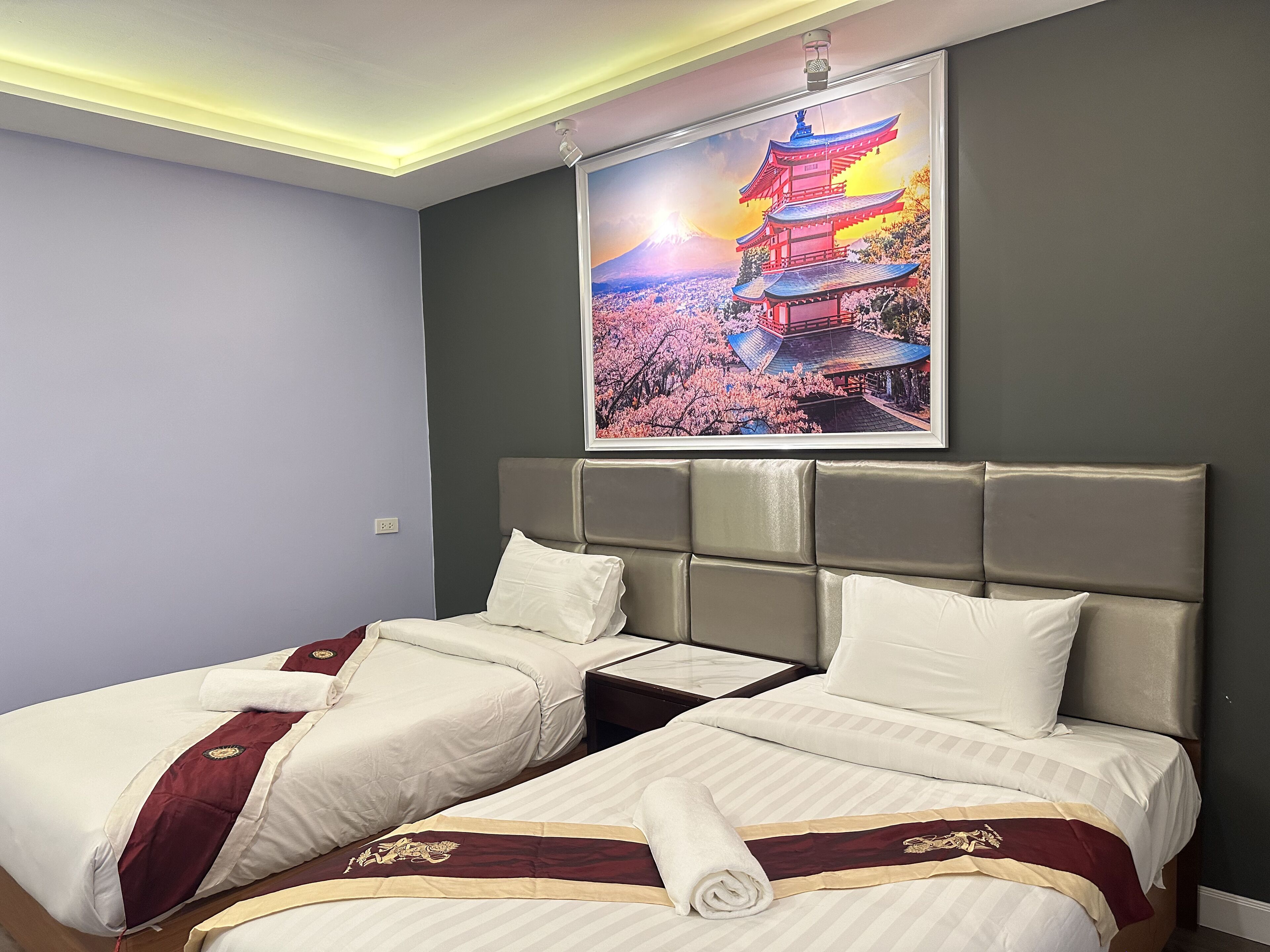 A hotel room with two beds, a large painting of a pagoda, and a modern ceiling design.