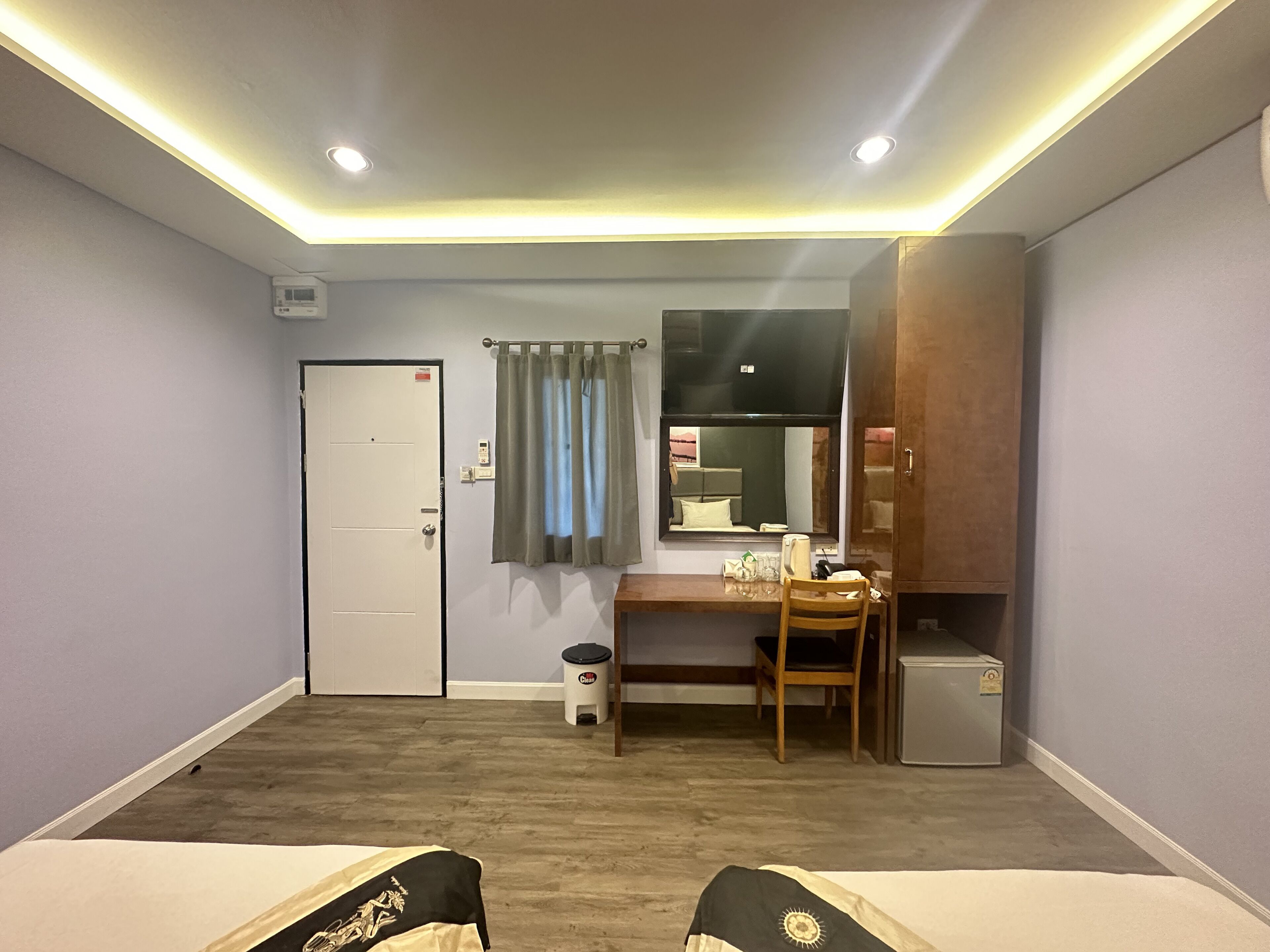 A hotel room with a bed, a desk, a chair, a wardrobe, and a small refrigerator.