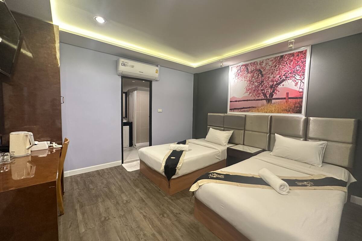 Quarto de hotel com duas camas, uma escrivaninha de madeira, um aparelho de ar condicionado e um quadro de uma cerejeira em flor.
