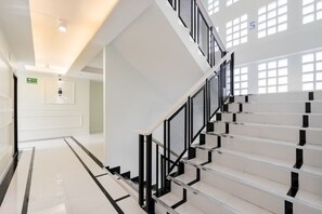 A modern staircase with black railings and white steps, leading to a bright area with natural light. - Metro Link Ratchada Hotel (Bangkok)