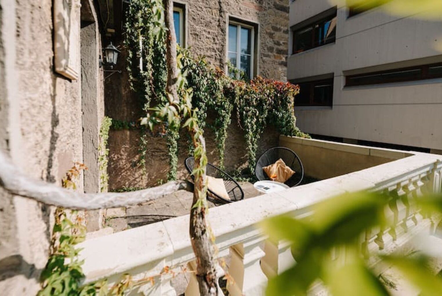 A balcony with a chair and a table, surrounded by greenery and a stone wall.