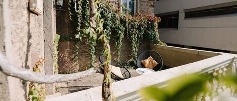 A balcony with a chair and a table, surrounded by greenery and a stone wall.