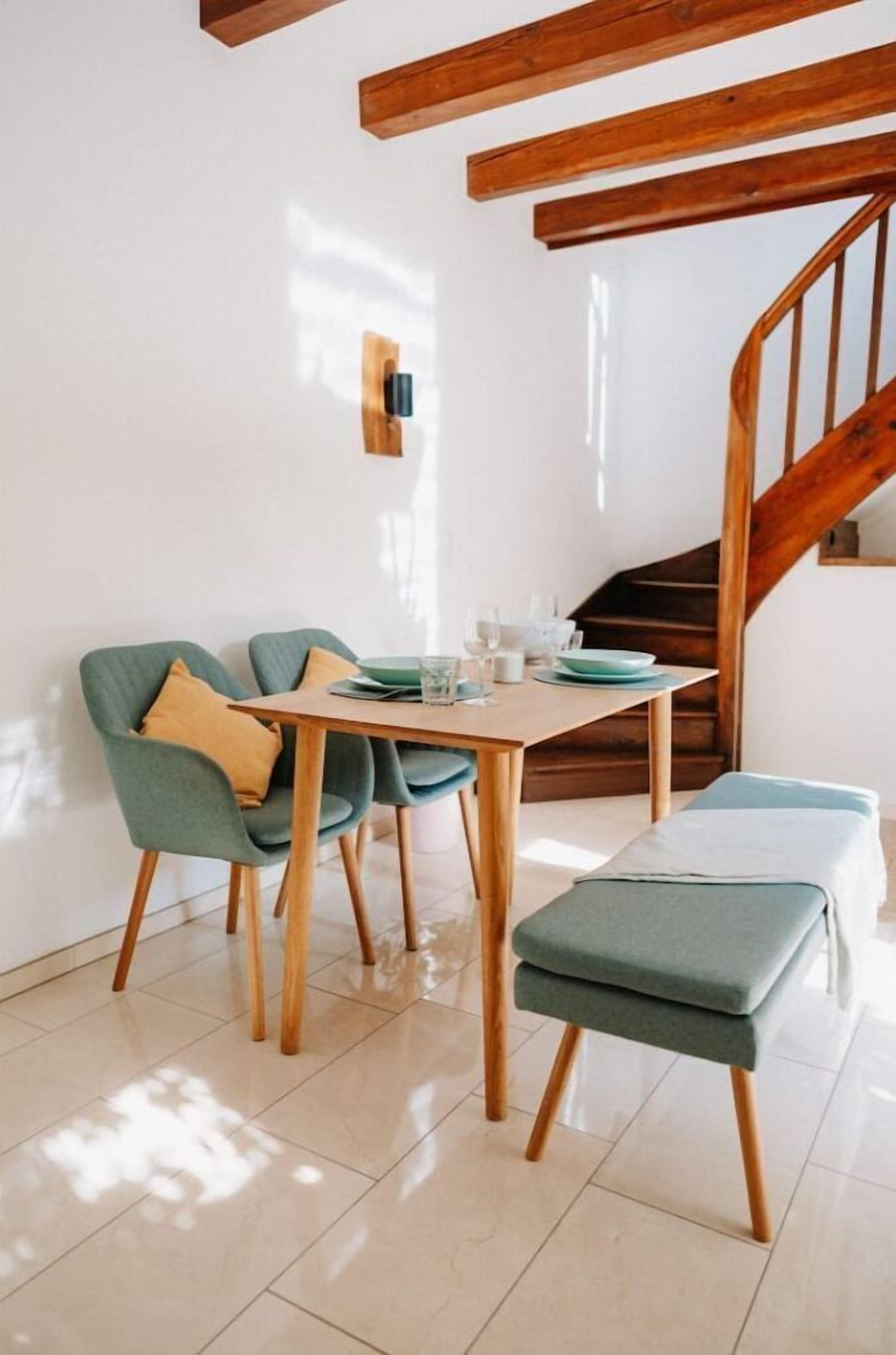 A dining area with a wooden table, two chairs, and a bench. A staircase is visible in the background.