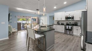 Una cocina moderna con gabinetes blancos, electrodomésticos de acero inoxidable y una isla central con taburetes de bar.