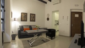 A modern living room with a sofa, coffee table, and a dining area. There is a kitchen visible in the background. - Apartamento Estándar (Sevilla)