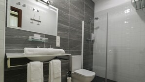 A modern bathroom with a white sink, mirror, and toilet, and a glass-enclosed shower area. - Apartamento Estándar (Sevilla)