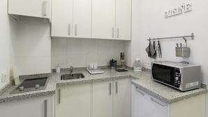 A compact kitchen with white cabinets, a granite countertop, a built-in microwave, and a coffee maker. - Apartamento Estándar (Sevilla)