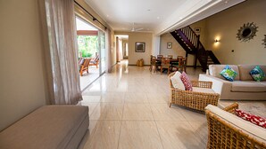 A spacious living area with a sofa, wicker chairs, a dining table, and a staircase. - Anse Boudin Villa (Praslin)