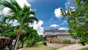 A modern house with a covered porch, surrounded by lush greenery and a clear blue sky. - Anse Boudin Villa (Praslin)
