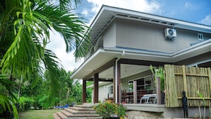 A modern house with a covered porch, a stone wall, and a garden with palm trees. - Anse Boudin Villa (Praslin)