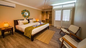 A bedroom with a bed, bedside tables, a ceiling fan, a window with blinds, and a wardrobe. - Anse Boudin Villa (Praslin)