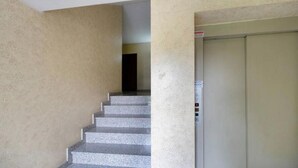 Una scala conduce a un ascensore in un edificio con pareti spoglie e una porta con un pannello di controllo.