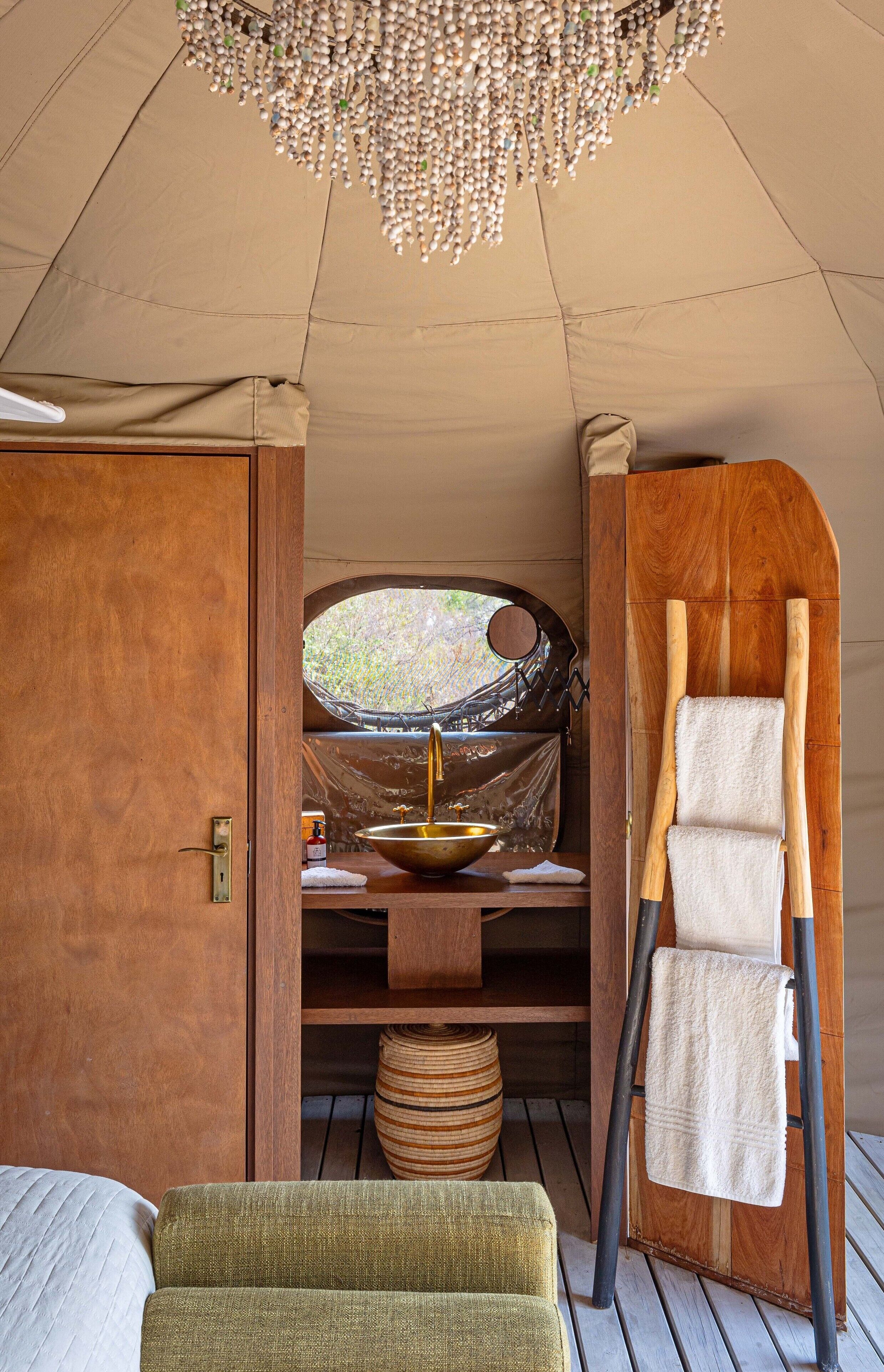A tent interior with a wooden door, a large window, a sink, a towel rack, and a bench.