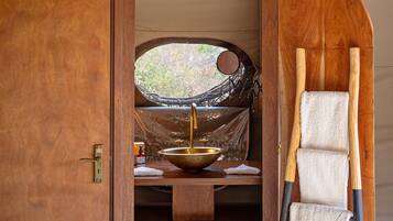 A tent interior with a wooden door, a large window, a sink, a towel rack, and a bench.