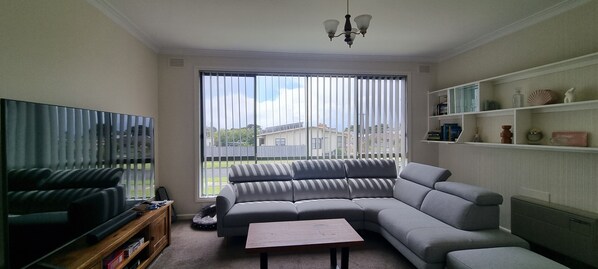 A living room with a sectional sofa, a television, a coffee table, and a bookshelf. - Henty Bay Hideaway Portland (Portland)