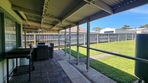 A covered patio area with a view of a fenced backyard, a grill, and outdoor seating.