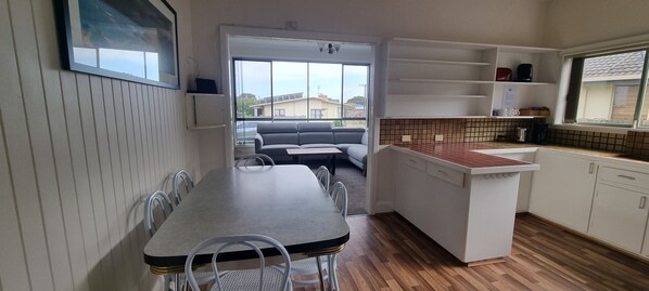 A compact kitchen with a dining area, a small island, and a view through an open door to a living space. - Henty Bay Hideaway Portland (Portland)
