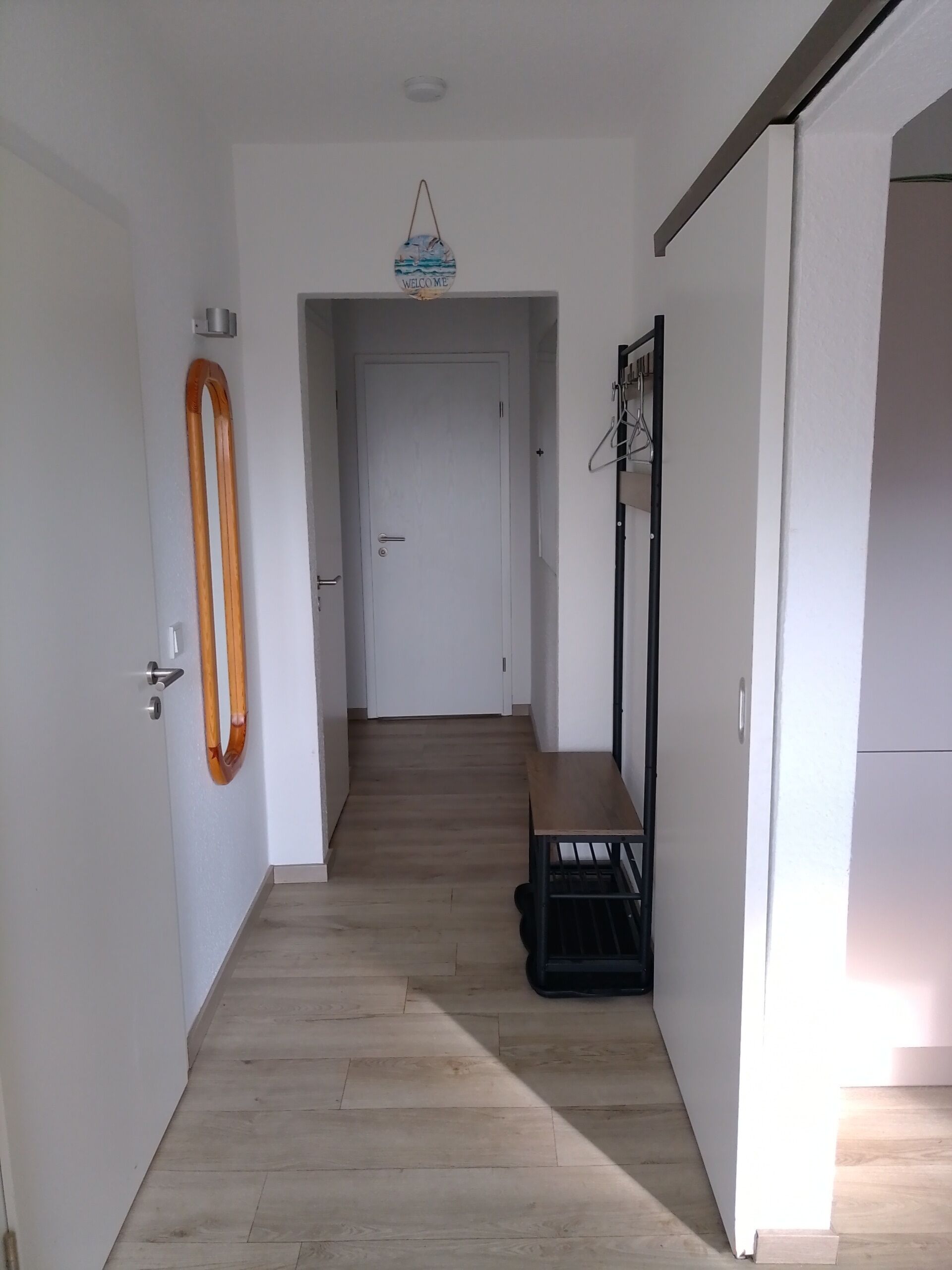Een gang met een houten bankje, een kapstok en een welkomstbord.