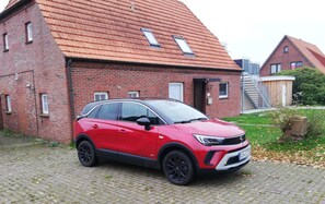 A red SUV parked in front of a red brick building with a sloped roof and a small staircase leading to a wooden door. - Ferienwohnung Amunds Koje Plus, Kinder-und Hundefreundl., Nähe Strand u Zentrum (Butjadingen)