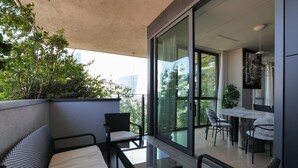 A balcony with wicker furniture, a dining table with chairs, and a view of greenery and buildings. - Luxury Suite in bosco Verticale Milano Isola  (Milano)