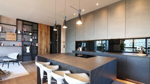 A modern kitchen with a central island, bar stools, pendant lighting, and a view of the city through large windows. - Luxury Suite in bosco Verticale Milano Isola  (Milano)
