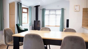 Ein Konferenzraum mit einem langen Tisch, Stühlen, einem schwarzen Kaminofen und einem Fenster mit Vorhängen.