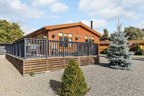 Une cabane en bois dotée d’une terrasse, entourée de gravier et d’un petit arbre à feuilles persistantes.
