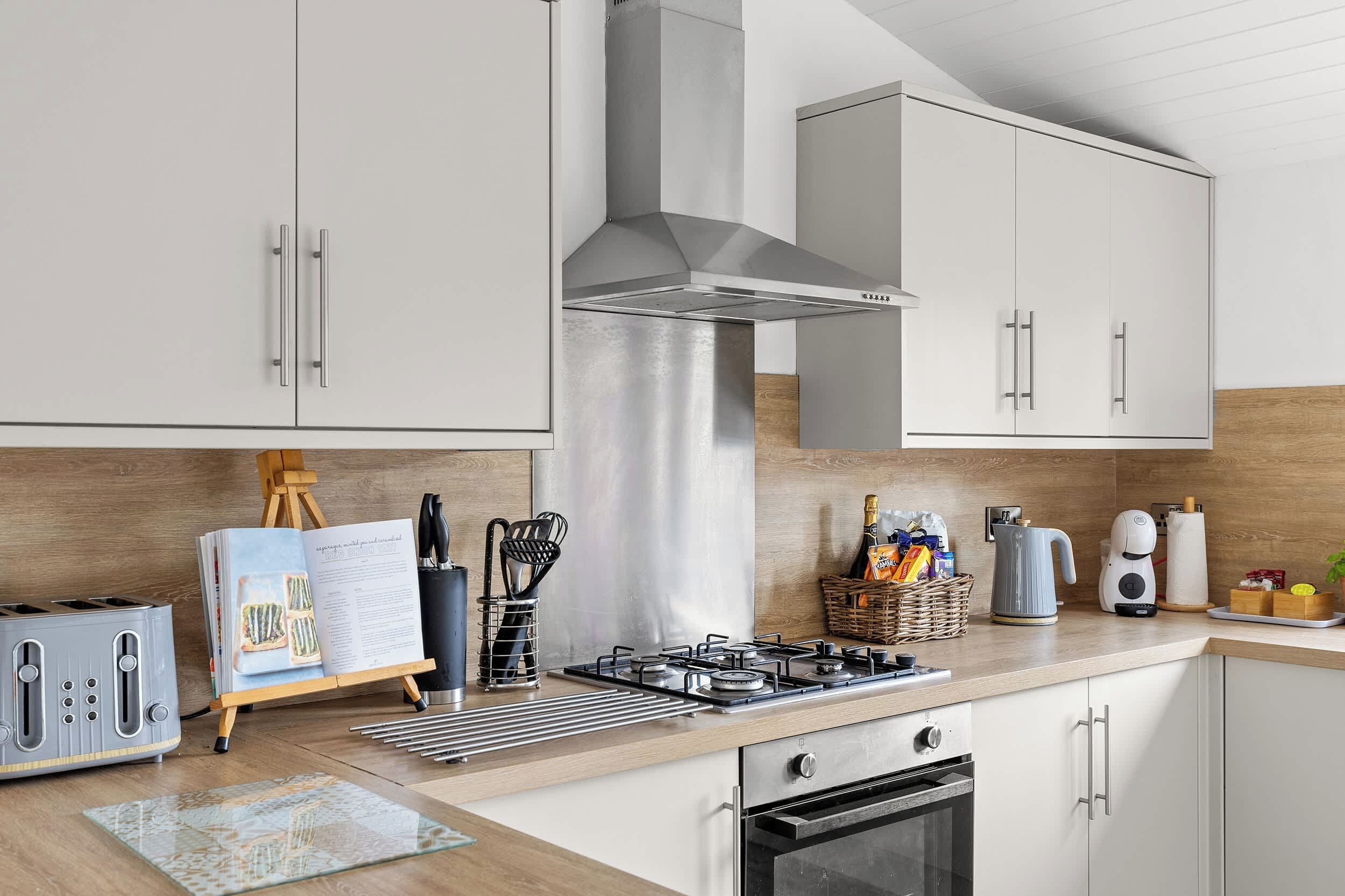 Een moderne keuken met witte kasten, een roestvrijstalen afzuigkap, een gasfornuis en een inbouwoven.