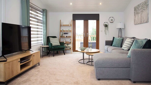 Ein Wohnzimmer mit Fernseher, einem grünen Sessel, einem grauen Sofa, einem Holzschrank und einem Bücherregal.