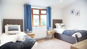 Ein Zimmer mit zwei Betten, einem kleinen Tisch, einem Heizkörper und einem Fenster mit Vorhängen.