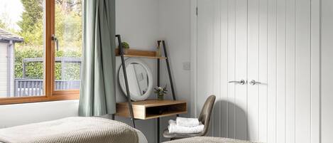A bedroom with two beds, a wooden shelf with decorative items, a chair, and a white door.
