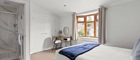 A bedroom with a bed, a desk, a chair, a window, and a door leading to a bathroom.