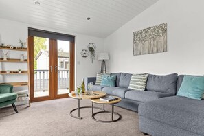 A modern living room with a grey sofa, a round wooden coffee table, and a green armchair. - Eagle Lodge - Luxury Lodge w/ Hot Tub near York (York)