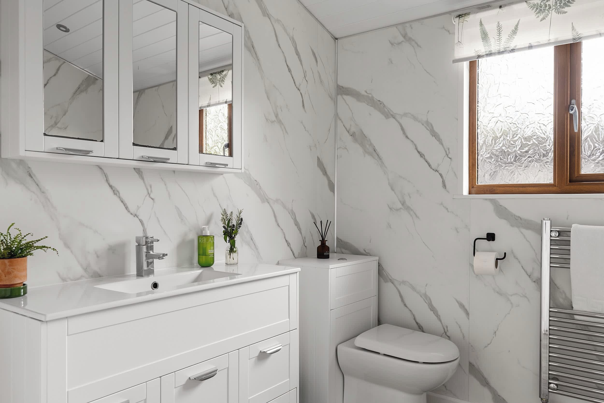 Une salle de bain avec un meuble-lavabo blanc, un miroir, des toilettes et une fenêtre en verre dépoli.
