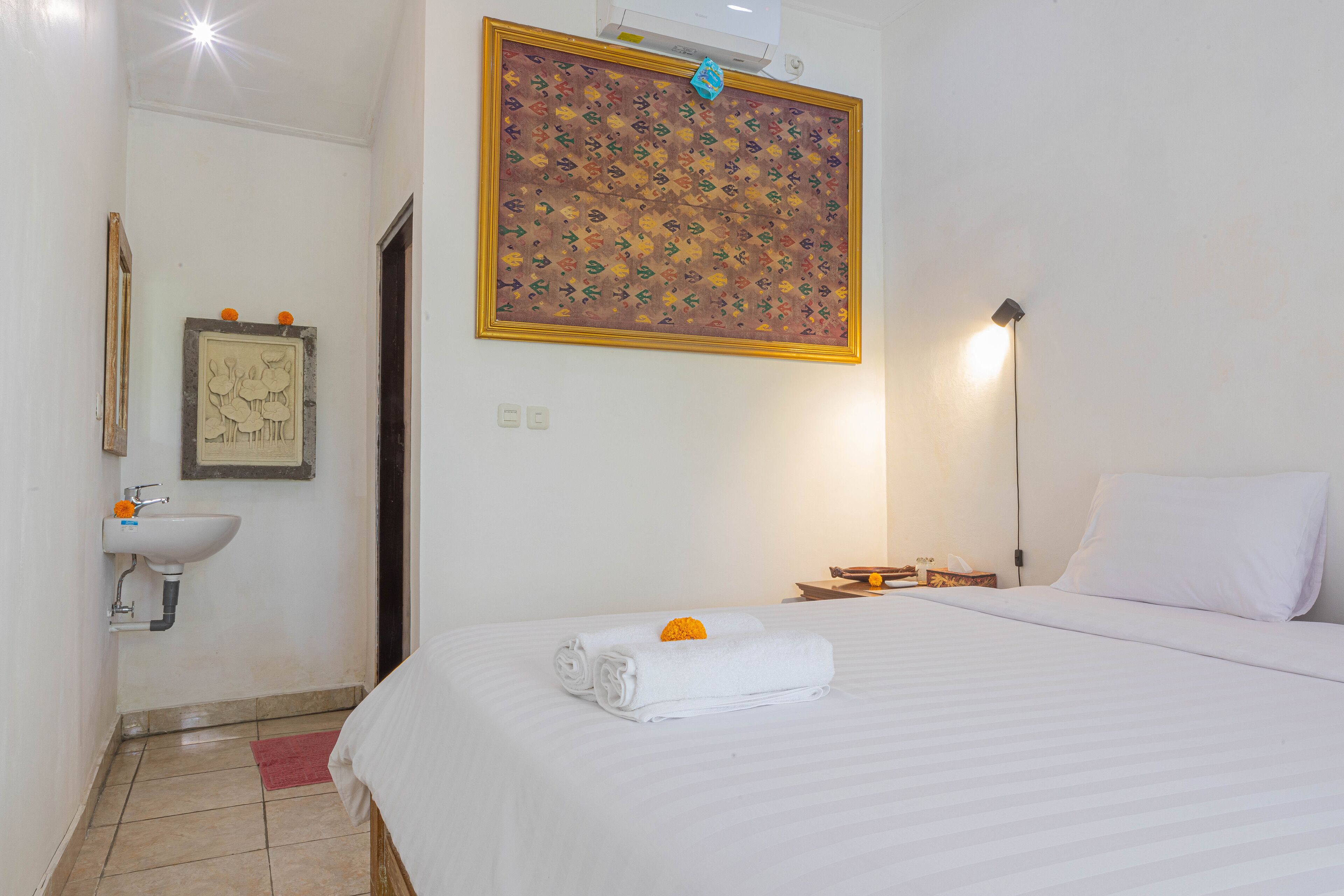 A hotel room with a bed, a sink, a framed artwork, and a wall-mounted air conditioner.