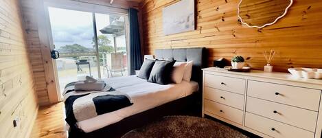 Ein Schlafzimmer einer Holzhütte mit Bett, Schminktisch und Blick ins Freie.