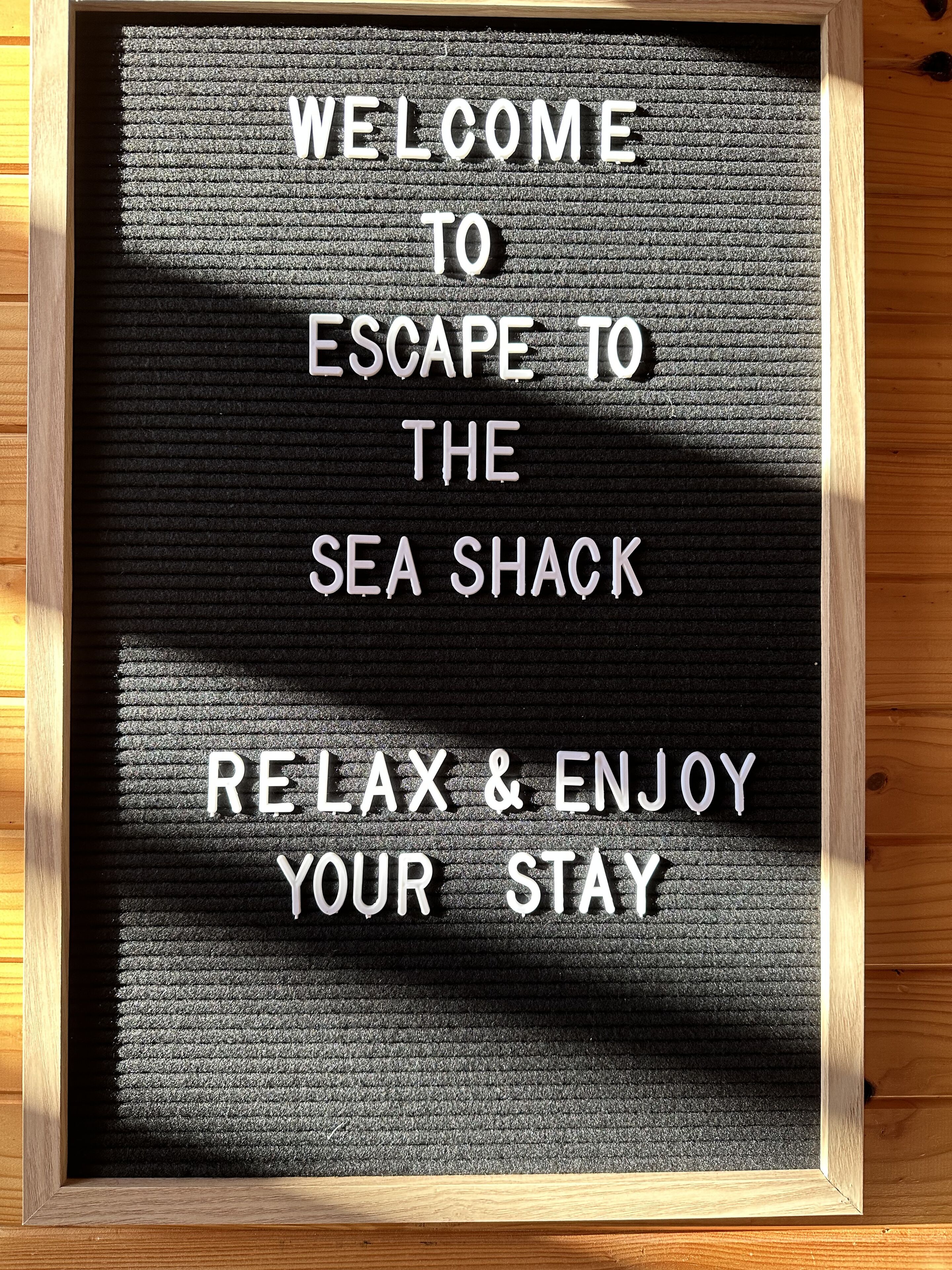 Ein gerahmtes Schild mit dem Schriftzug: 'WELCOME TO ESCAPE TO THE SEA SHACK RELAX & ENJOY YOUR STAY'.
