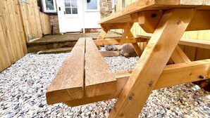 Ein Holztisch für ein Picknick in einem Innenhof mit einer Steinmauer und einer weißen Tür im Hintergrund.