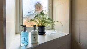 Ein Badezimmer mit Fenster, einer Topfpflanze und zwei Flaschen Shampoo und Conditioner auf dem Fensterbrett.