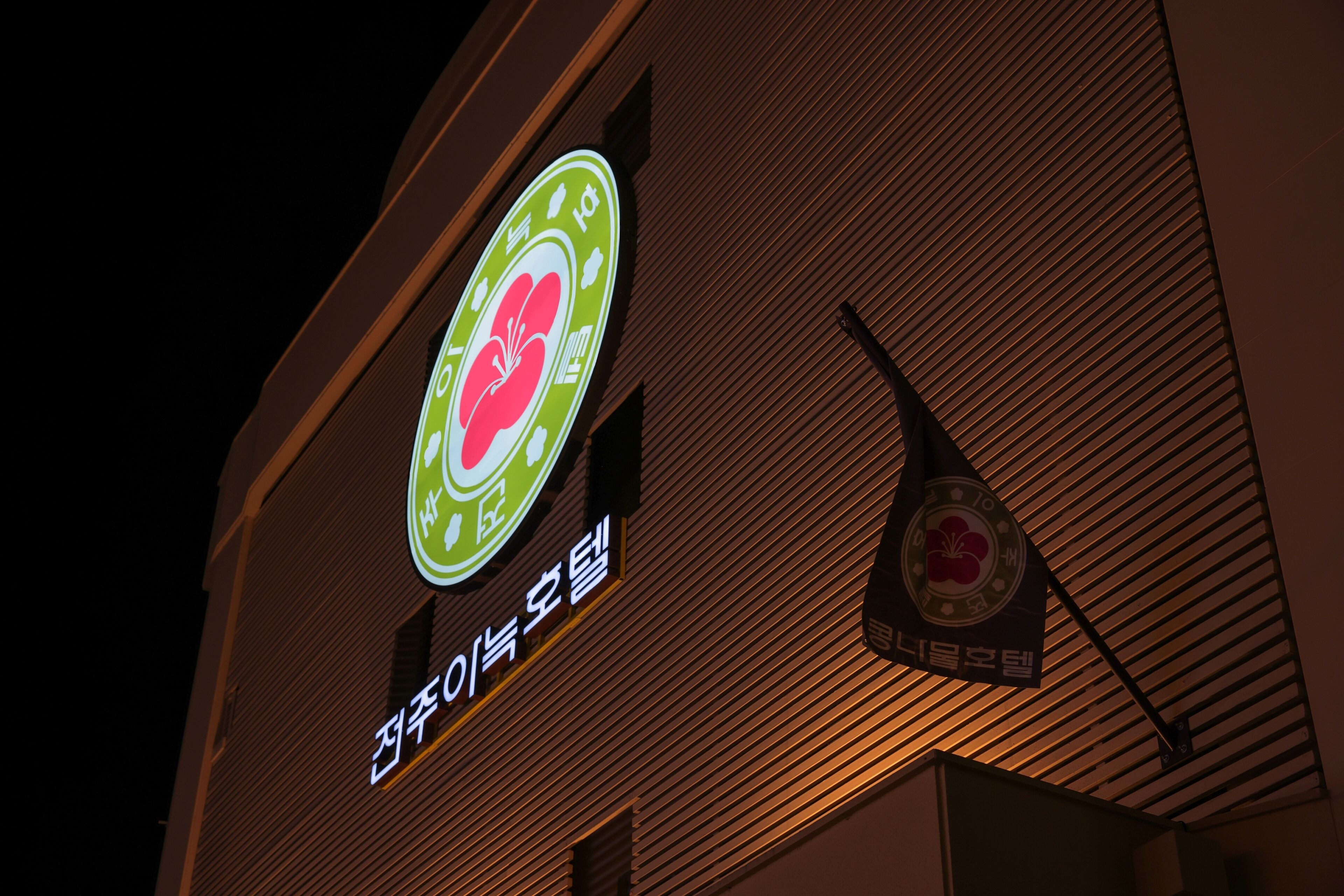 A building with a sign featuring a green and white logo with a red flower, and Korean text.